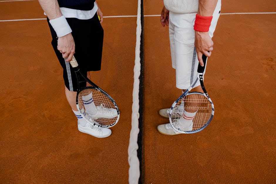 Two tennis players stand on a clay court with rackets, ready for a match.